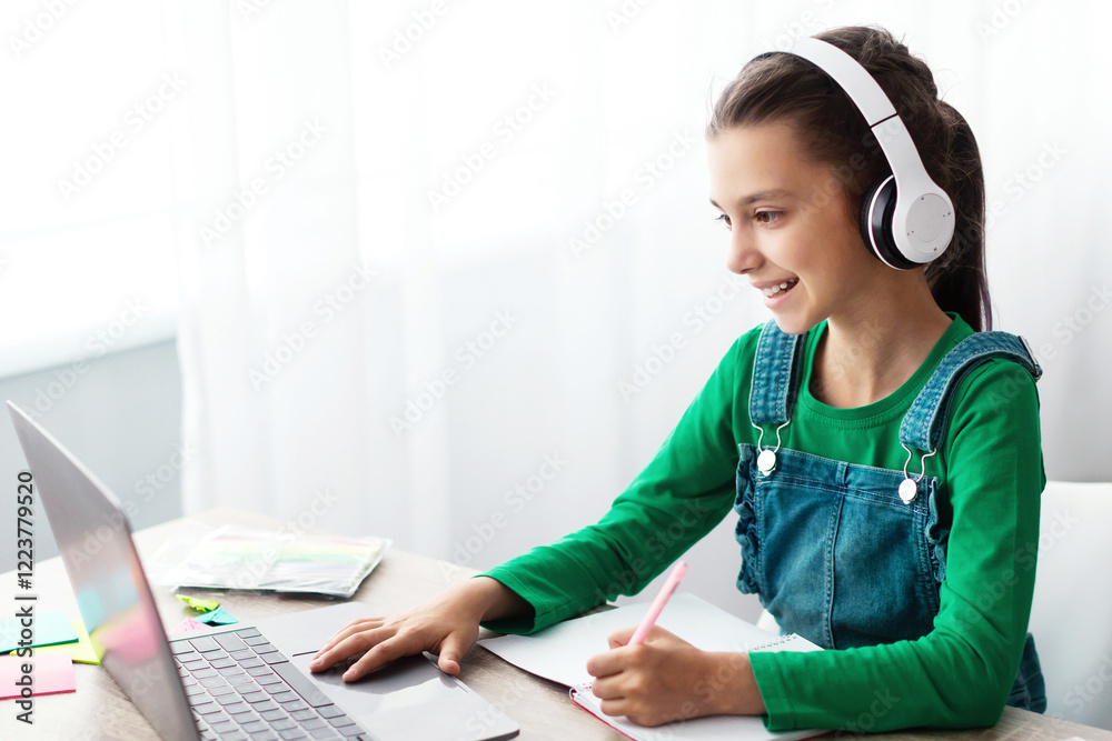 Poster Studying At Home. Cheerful schoolgirl doing homework and typing on keyboard, sitting at table using laptop, looking at screen, writing essay or making test, taking notes in textbook, free copy space