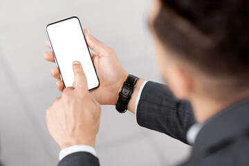Unrecognizable Man Using Smartphone With Blank White Screen While Sitting With Luggage Outdoors,...
