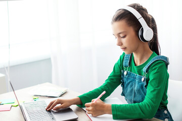 Educational Lecture Concept. Portrait of diligent teen girl in wireless headphones sitting at table...