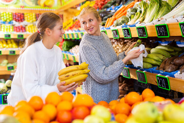 Portrait of cheerful friendly teenage girl and her mother during family shopping in fruit store..
