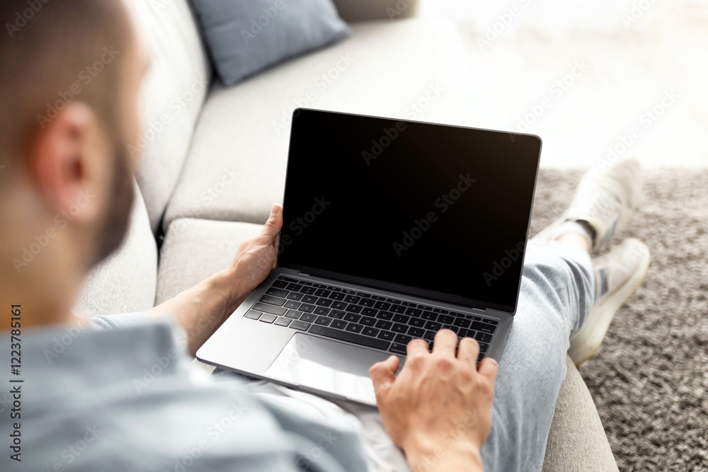 Poster unrecognizable young man using laptop on comfy sofa at home, mockup for website design on screen. mi