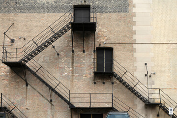 Two black metal fire escapes zigzagging down a brick wall with closed doors at the top