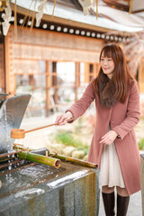 A shrine in Hakata, Fukuoka, Japan. A Japanese woman with a long hair in her thirties cleans her hands using a ladle.