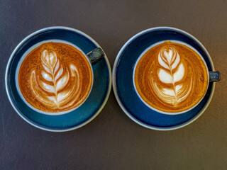 Barista concept, Selective focus of a coffee cup on the table with dark tone, Hot cappuccino or latte art with milk foam on the top, Drinking coffee at the cafe' in the afternoon, Beverage background.