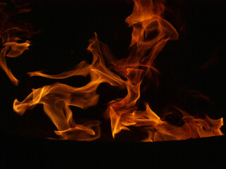 Close-up of dynamic flames on a black background, showcasing vibrant orange and yellow hues. Abstract patterns created by the movement of fire, symbolizing energy, heat, and the raw power of nature.