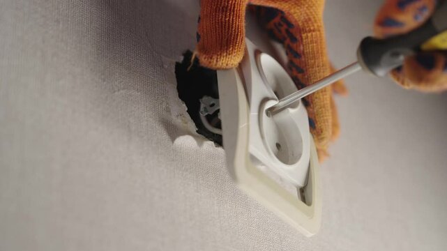 Electrician with Wrong Screwdriver Trying to Fix Loose Wall Socket, Common Household Repair Mistake with Electric Outlet