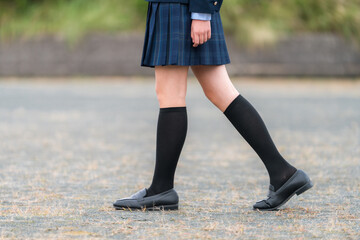学校の校庭・グランドを歩くブレザー姿の女子生徒の足元
