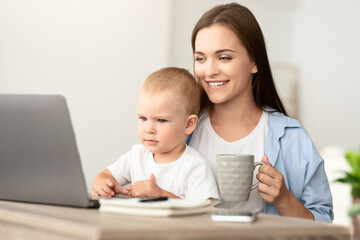 Technology And Childcare. Mother Drinking Tea While Baby Watching Cartoons On Laptop, Happy Young Mom With Toddler Son On Hands Relaxing At Home With Computer, Closeup Shot With Free Space