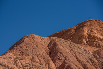 view of a person climbing in a red mountain heading to a cross in the top, winning in hiking reaching life goals, success, freedom and toughness