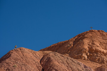 view of a person climbing in a red mountain heading to a cross in the top, winning in hiking reaching life goals, success, freedom and toughness