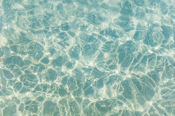 Rippled surface of clear turquoise water with sunlight reflections creating a sparkling natural pattern.
