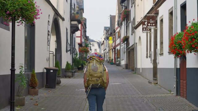 Rear view of solo tourist with heavy backpack walking through a narrow German street by herself as we follow behind