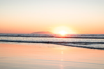 Sunrise scene at the beach over Pacific ocean  - sun coming from behind the waves lighting up the clear sky with bright yellow and orange colors. El Cuco Beach, El Salvador.
