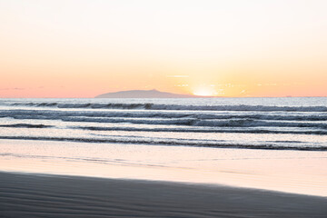 Fototapeta premium Sunrise scene at the beach over Pacific ocean - sun coming from behind the waves lighting up the clear sky with bright yellow and orange colors. El Cuco Beach, El Salvador.
