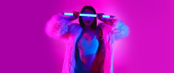 Toned portrait of beautiful young woman with neon lamp on bright background
