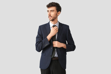 Young businessman in suit fixing necktie on light background