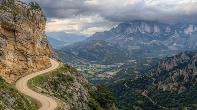 A winding dirt road snakes along the edge of a rocky cliff, leading into the breathtaking expanse of rugged mountains and lush valleys under a brooding sky filled with clouds.