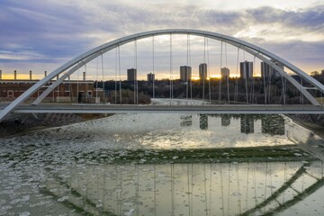 Sunrise over the icy river, modern Walterdale Bridge reflecting in the water. City skyline in the background.Edmonton, Alberta, Canada