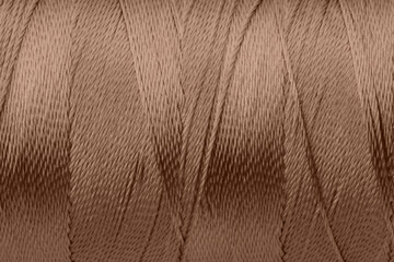 Sewing thread in mocha mousse shade, closeup. Trendy color of 2025 year
