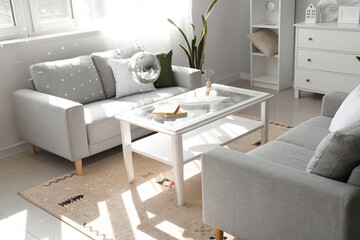 Interior of modern living room with grey sofas, hanging disco ball and coffee table