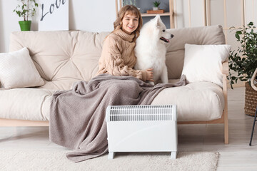 Young woman with plaid and her Samoyed dog on sofa warming near radiator at home