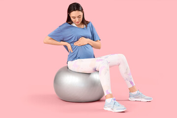 Beautiful young pregnant woman sitting on fitball against pink background