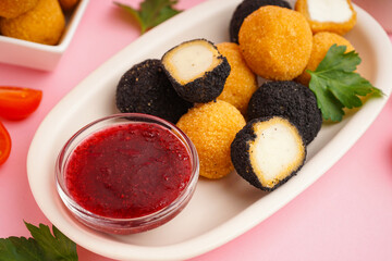 Plate with different delicious fried mozzarella balls and sweet sauce on pink background, closeup