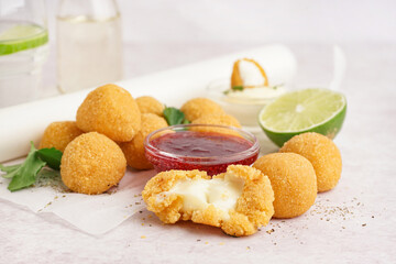 Paper with delicious fried mozzarella balls, sweet sauce and lime on light background, closeup