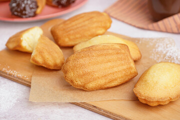 Wooden board with baking paper and delicious madeleines on white background