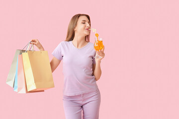 Beautiful young woman with shopping bags and cocktail on pink background