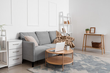 Stylish interior of living room with grey sofa and modern laptop on table