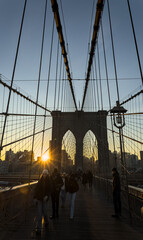 Fototapeta premium brooklyn bridge at sunrise (new york city landmark over east river to manhattan) travel tourism famous destination in usa america united states (suspension cables lamp light streetlight) people cross