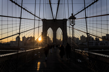 Fototapeta premium brooklyn bridge at sunrise (new york city landmark over east river to manhattan) travel tourism famous destination in usa america united states (suspension cables lamp light streetlight) people cross