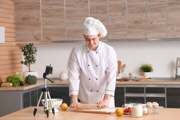 Male chef with dough and fruits recording cooking video in kitchen