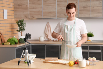 Male chef with dough and fruits recording cooking video in kitchen