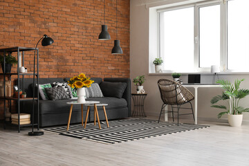 Cozy sofa, coffee table with sunflowers and workplace in interior of living room