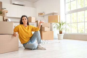 Beautiful woman with key from new flat and boxes sitting in kitchen on moving day