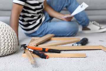 Tools with disassembled table on carpet against man with manual at home, closeup
