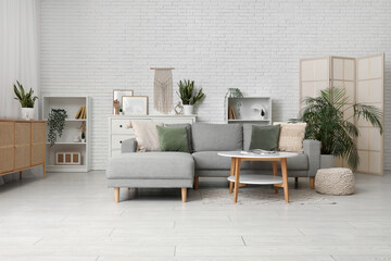 Interior of living room with sofa, pouf and table near white brick wall
