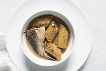Overhead view of Nigerian pepper soup with fish and plantain in a white soup plate, top view of fish pepper soup in a white plate