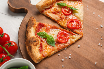 Cutting board with pieces of tasty pizza Margarita on white wooden background, closeup
