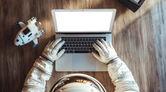 An astronaut is typing on a laptop with an empty white screen. There is a rocket model on the table next to the laptop. A mockup of a stylish laptop. Cosmonautics Day is April 12