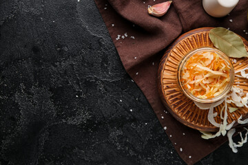 Glass jar with homemade sauerkraut on napkin on black background. Top view