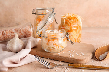 Glass jars with tasty sauerkraut and bottle of salt on table against beige background. Closeup