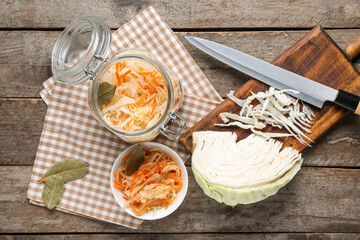 Glass jars and bowl with tasty sauerkraut and cabbage on wooden background. Top view