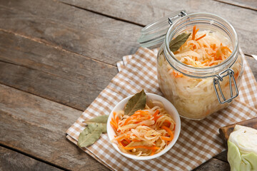 Glass jars and bowl with tasty sauerkraut on wooden background. Closeup