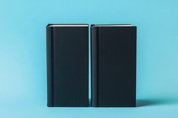 shot of two black books with plain covers, standing upright on a light blue background