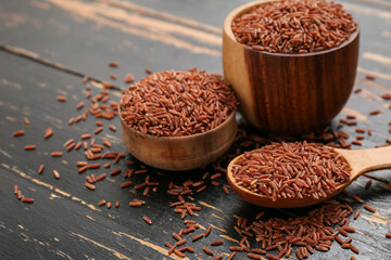 Bowls and spoon with raw brown rice on dark wooden background