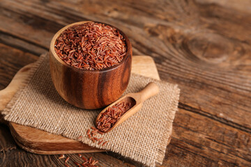 Board with bowl and scoop of raw brown rice on wooden background