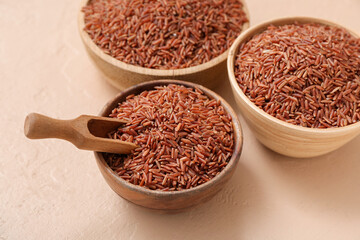 Wooden bowls with raw brown rice and scoop on beige background